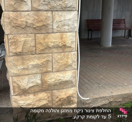 קיר אבן עם צינור חשוף ליד עמוד ובספסל